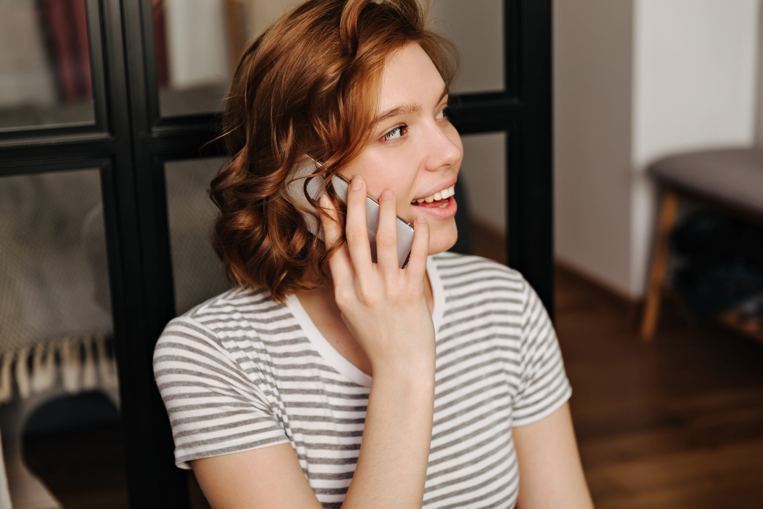 Closeup portrait of red curly girl in striped t-shirt talking on phone.